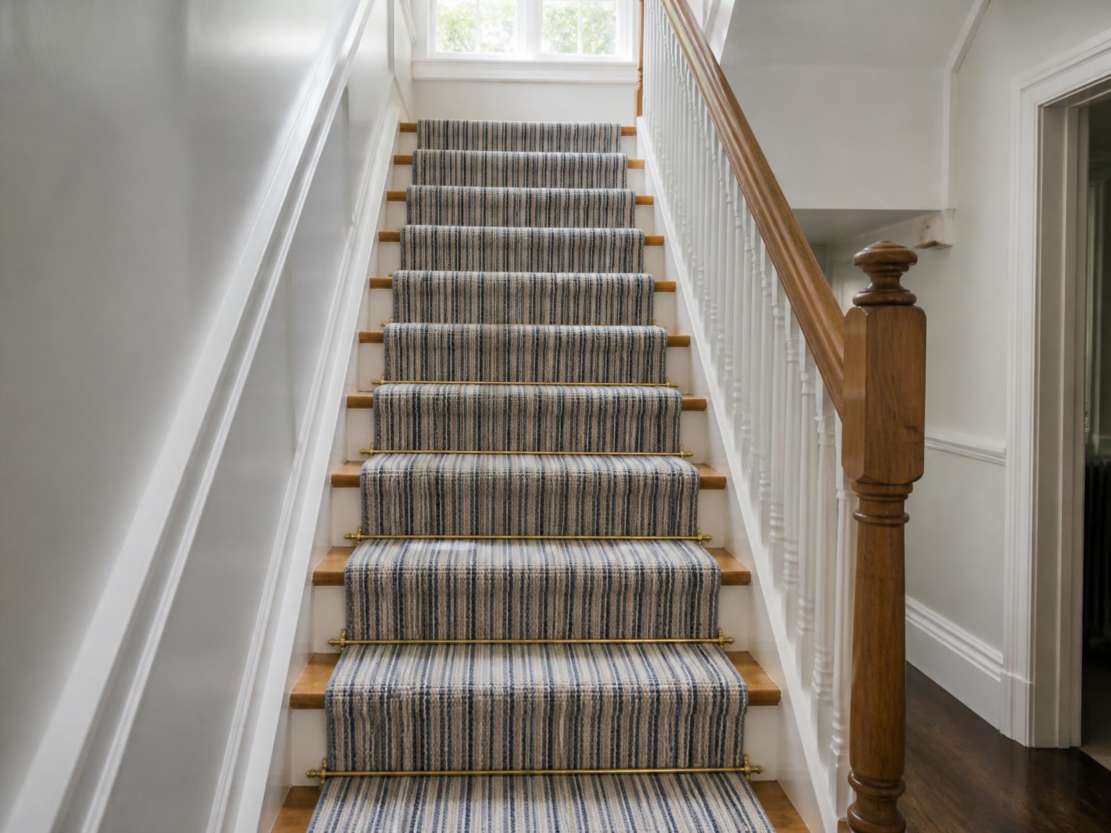 Striped stair runner neatly fitted with brass stair rods on a bright staircase
